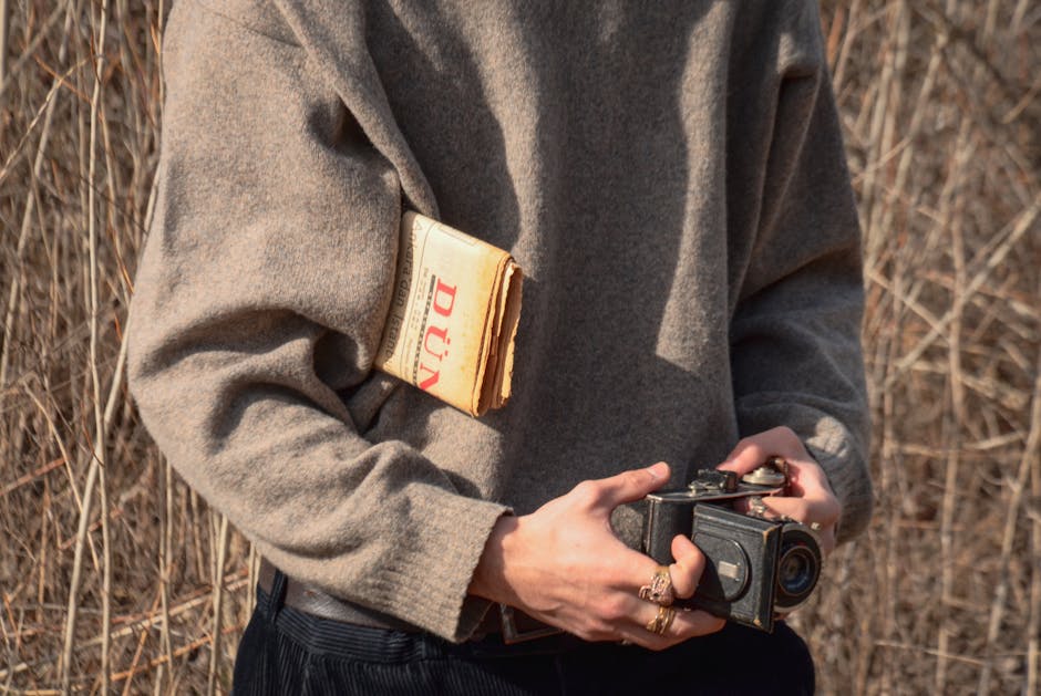 Close-up of a person holding a vintage camera with newspaper outdoors. Warm autumn tones.